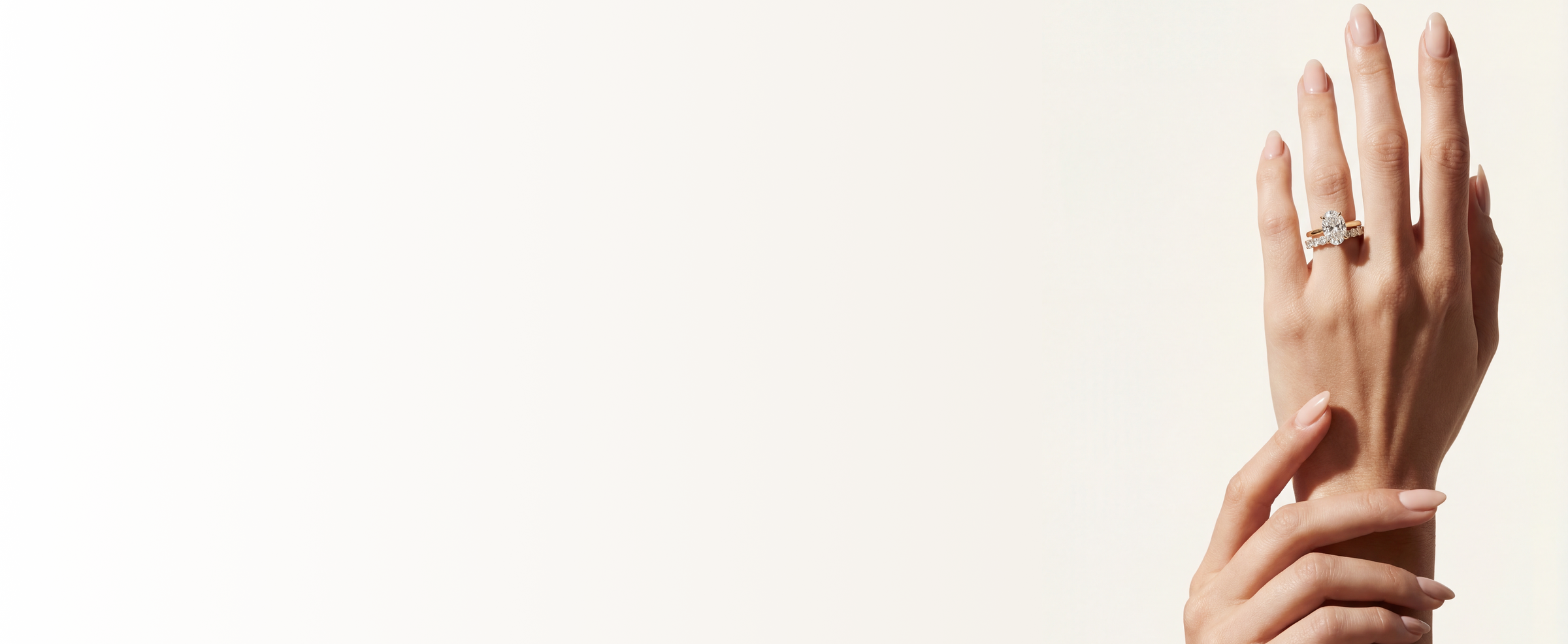 Model's hand wearing an engagement ring and wedding band on a plain background